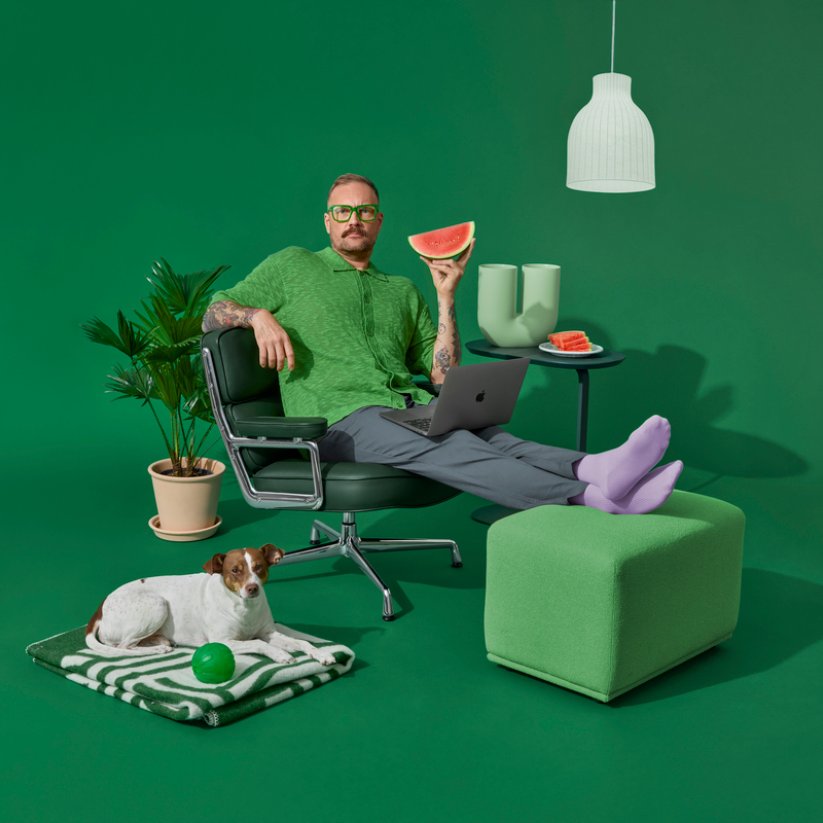 Een man zit op een stoel, met een hond naast hem op de grond.